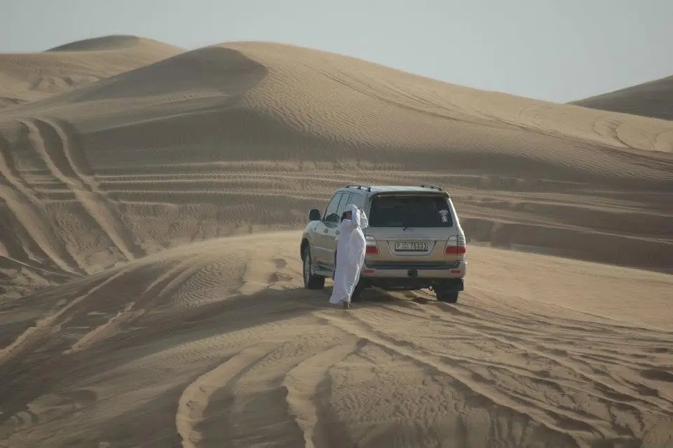 Geländewagen und zwei Personen in traditioneller Kleidung in den Dünen bei Dubai