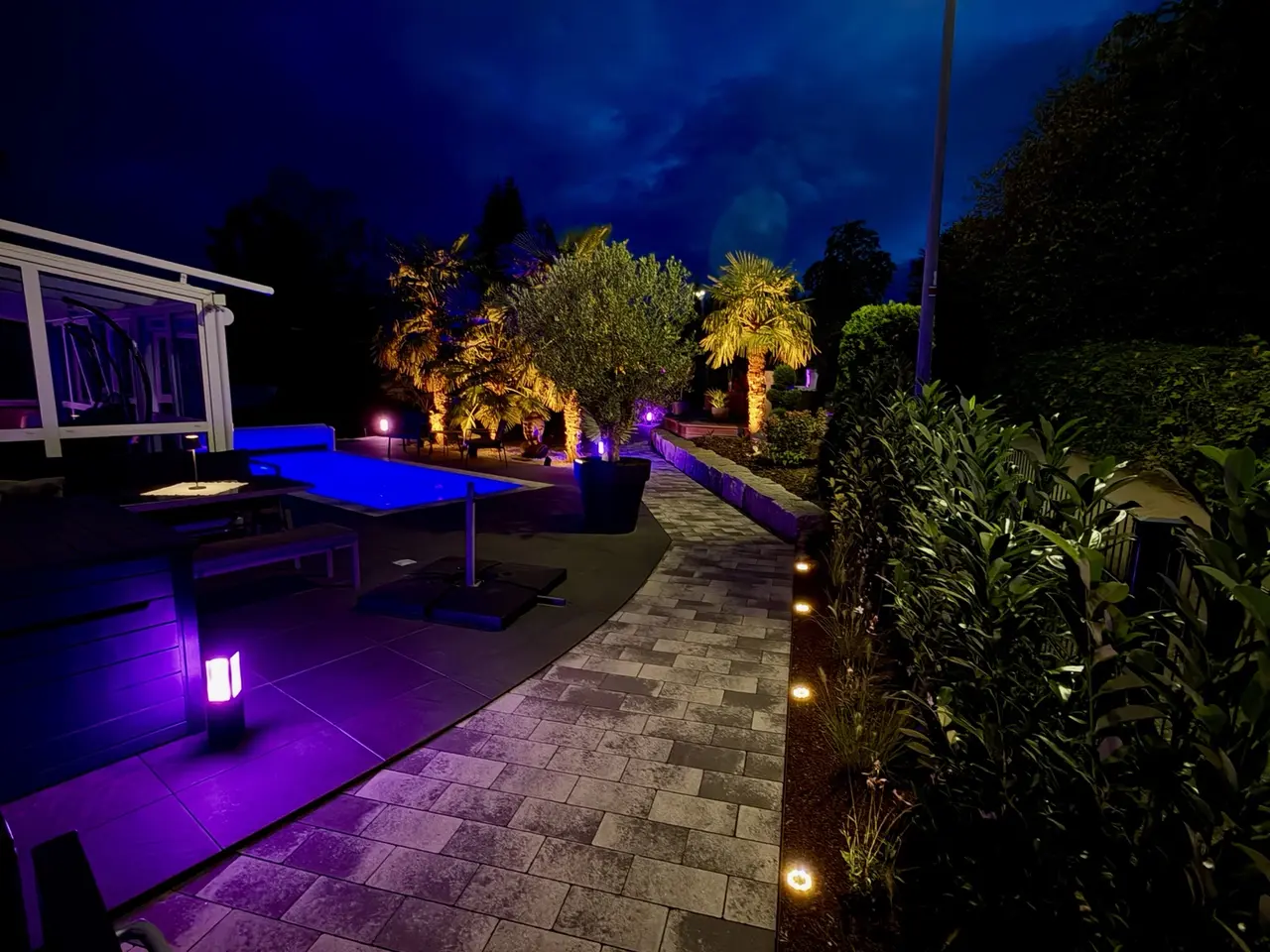 Beleuchteter Weg durch den Garten neben Pool und Pflanzbeeten