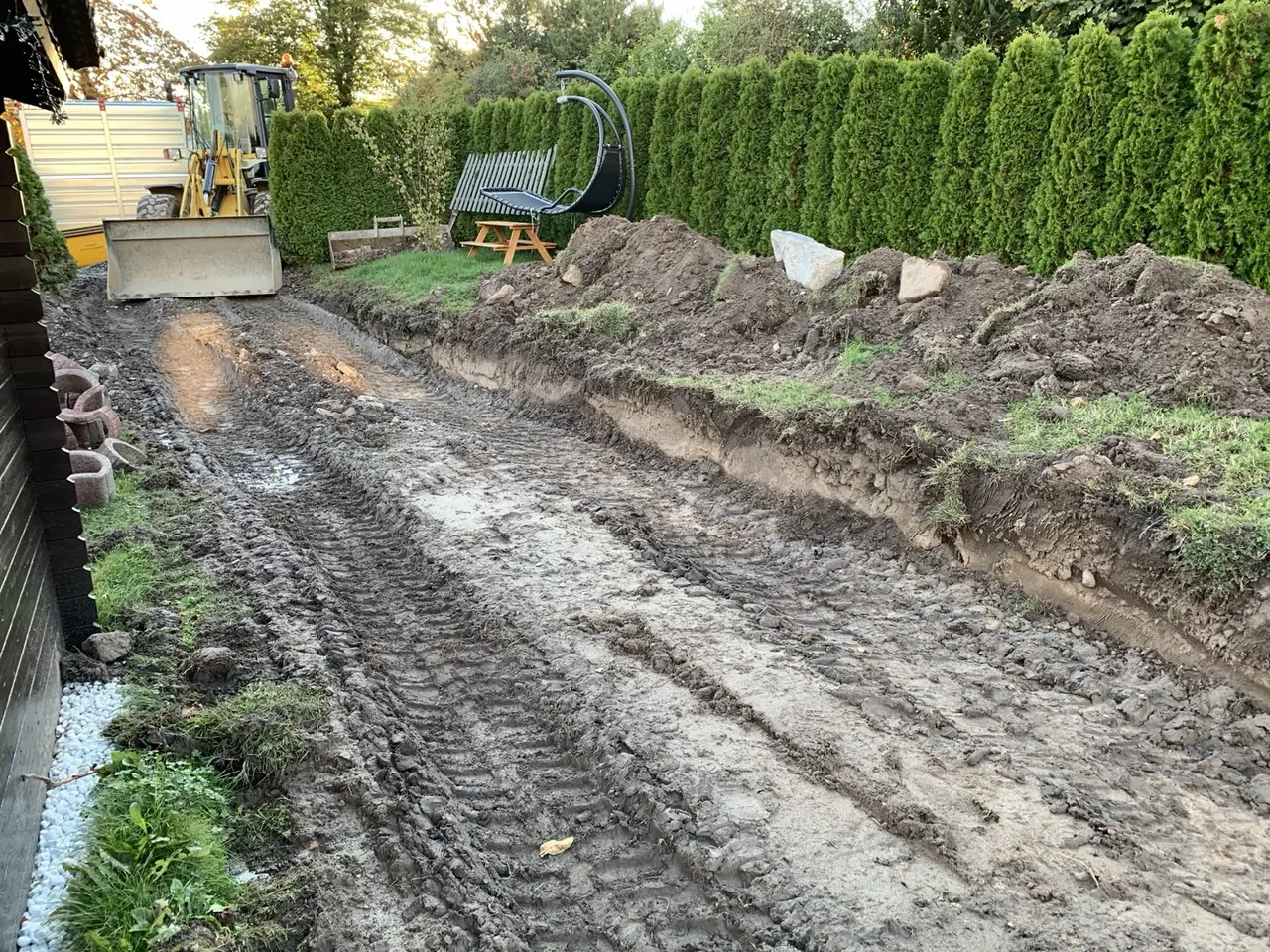 Ausgehobene Fläche mit Erdspuren und Bagger im Garten