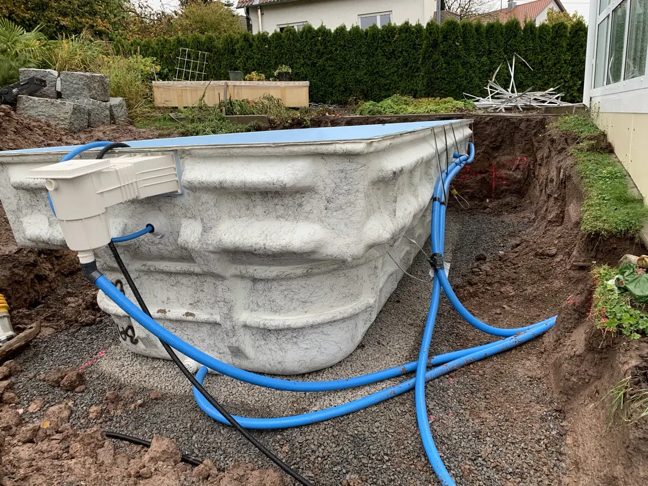 Eingesetztes Poolbecken mit vorbereiteten blauen Leitungen in der Baugrube