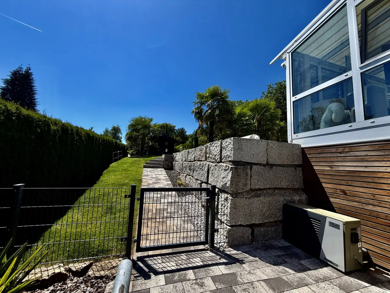 Gartenweg entlang einer Natursteinmauer und eines Wintergartens