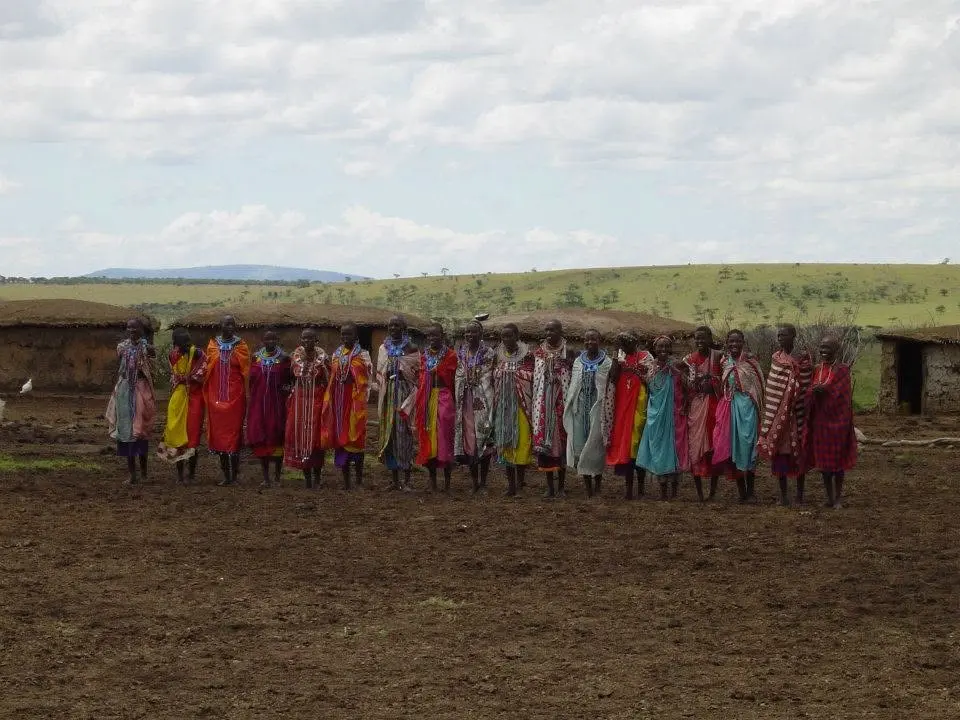 Gruppe von Menschen in farbenfroher traditioneller Kleidung vor Häusern in Kenia
